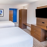 Two bed bedroom with television, desk, chair, and office lamp.