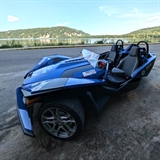 A slingshot vehicle in front of a large lake.